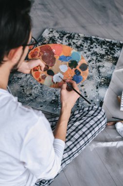 Genç adam, kendini izole etme üzerine bir resim çizmek için yağlı boyaları ahşap bir palette karıştırıyor. Sanat terapisi. Ev tatili. resim atölyesi