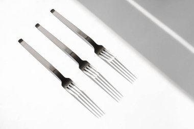 Beyaz bir zemin üzerinde çatal seti ve güneş ışınlarından gelen sert gölgeler. Üst görünüm yakın plan. Çatal bıçak. Konu fotoğrafçılığı. soyutlama