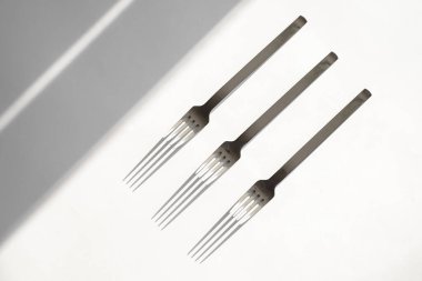 Beyaz bir zemin üzerinde çatal seti ve güneş ışınlarından gelen sert gölgeler. Üst görünüm yakın plan. Çatal bıçak. Konu fotoğrafçılığı. soyutlama