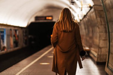 Metroda paltolu genç bir kadın arabasını bekliyor. Kız metro istasyonuna koruyucu bir maskeyle gidiyor. salgın 2021