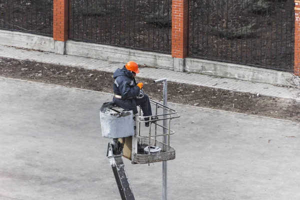 male worker changes a lamp in a street light. an electrician in uniform works on a telehandlers