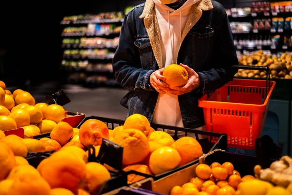 a man in a protective mask in a supermarket chooses fruits and citrus fruits. man during a pandemic buys groceries in the store. courier picks up an order in a supermarket
