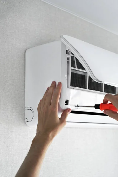 a man repairing an air conditioner at home. technician repairman. the man unscrews the screw in the air conditioner for cleaning.