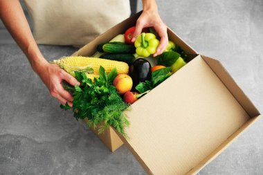 a girl unpacks a parcel from a store with vegetables and fruits. online delivery of goods to your home. vegetables in a box close-up