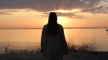 Şafak vakti, arka planda deniz olan yamaçta yürüyen genç bir kadın.