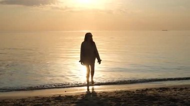 Deniz kıyısında yürürken şafağı selamlayan genç bir kadının portresi.