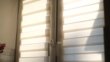 Güneşli bir sabahta bir adam pencerenin perdesini açar.