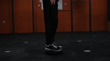 Siyah takım elbiseli bir adam spor salonunda denge küresi üzerinde duruyor ve yan görüş egzersizleri yapıyor.