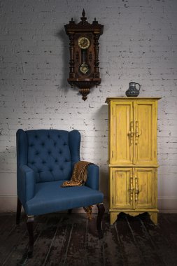 Vintage mavi koltuk, sarı dolap, sarkaç saat ve turuncu eşarp
