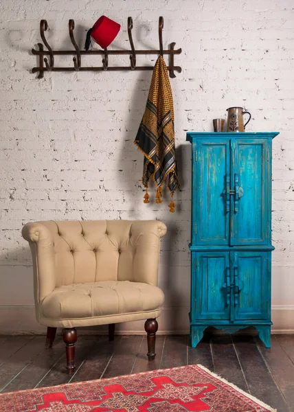 Classic beige armchair, vintage turquoise cupboard, and wall hanger with ornate scarf on bricks wall