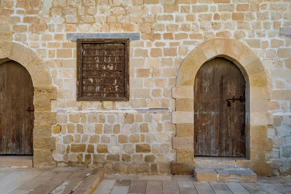 Two weathered wooden arched doors and closed rusted wrought iron windows on bricks stone wall