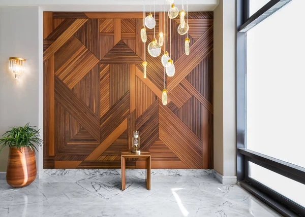 Ahşap kaplama duvar, çalılı uzun saksı, modern cam uzun avize ve beyaz mermer zemin.