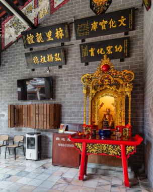 Kuala Lumpur, Malaysia - Feb. 21, 2025: Chan She Shu Yuen Ancestral Hall interior. Golden altar, red offering table, and traditional Chinese calligraphy on a grey brick wall