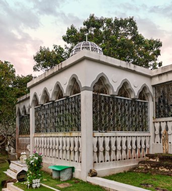 Royal Mausoleum, or Kubah Makam Diraja, in Bandar Seri Begawan, Brunei Darussalam. White building with a dome, intricate grilles, and surrounding tombs under a cloudy sky