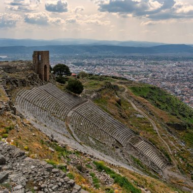 Türkiye 'nin Bergama kenti ve bulutlu bir gökyüzünün altındaki uzak dağlarla, Antik Yunan Pergamon harabelerinin panoramik manzarası.
