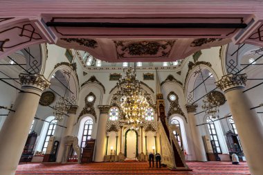 İzmir, Türkiye - 31 Mart 2025: Hisar Camii İçişleri. İslami mimariyi büyük avize, mihrab ve minbar ile süsleyin. Tapanlar sütunların ve vitrayların arasında kırmızı halıda dua ederler.
