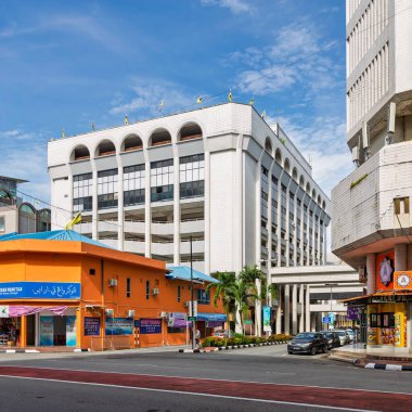 Bandar Seri Begawan, Brunei - 24 Şubat 2025: Jalan Sultan sokak sahnesi. Mavi gökyüzünün altında kemerli, turuncu bir dükkan, arabalar ve palmiye ağaçları olan modern beyaz bir bina.