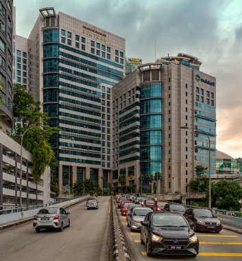 Kuala Lumpur, Malezya - 28 Şubat 2025: Bulutlu bir gökyüzü altında Plaza Sentral, Malakoff, SSM ve Axiata gibi modern binaların bulunduğu bir yolda trafik