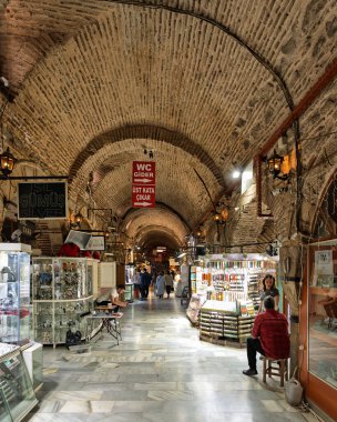 İzmir, Türkiye - 31 Mart 2025: Kizlaragasi Han Bazaar iç mimarisi. Tarihi kemerli taş tavan, mermer zemin ve mücevher ve aksesuar satan hareketli dükkanlar. İnsanlar markette yürür.