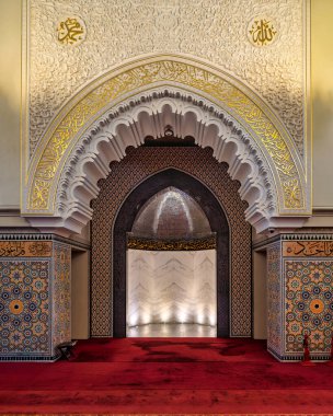 Ash Shaliheen Camii 'nin içi, Bandar Seri Begawan, Brunei. Altın Arap kaligrafisi, karmaşık oymalar ve mihrab 'a giden renkli geometrik fayanslarla süslü kemer yolu.