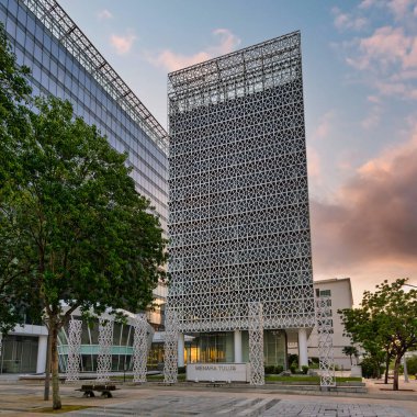 Menara Tulus, geometrik cepheli modern bir bina, Putrajaya, Malezya 'da altın saatinde cam bir yapı ve ağaçların yanında..