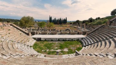 Türkiye 'nin Bergama, Pergamon Asclepieion kentindeki Antik Roma Tiyatrosu. Bulutlu gökyüzünün altında tarihi taş kalıntıları, sahne ve sütunlar.