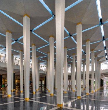Mescid Negara, Ulusal Cami Namazı, Kuala Lumpur, Malezya. Beyaz sütunları, geometrik tavanı, mavi ışık şeritleri ve yansıtıcı zemini olan modern iç mekan.