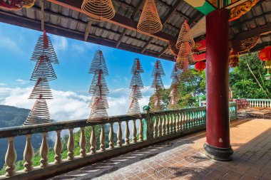 Spiral tütsü bobinleri Malezya, Genting Highlands 'daki Chin Sweet Caves Tapınağı' nda asılı. Tapınağın balkonunda sisli dağlar ve mavi gökyüzü görünüyor.