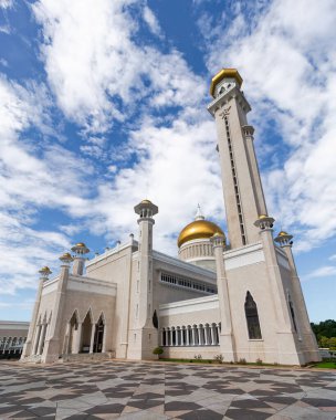 Omar Ali Seydien Camii, Bandar Seri Begawan, Brunei. Altın kubbeli, uzun minareli ve bulutlu mavi gökyüzünün altında desenli kaldırımlı görkemli caminin alçak açılı görüntüsü.