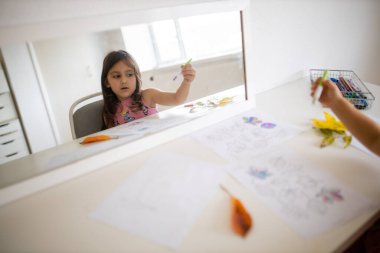 Farklı türde yaprakları kalemle boyayan küçük bir kızı yansıtan ayna.