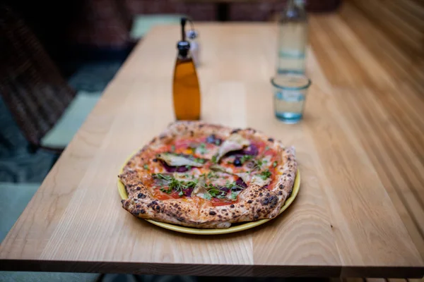 Vegan pizza on a table alongside a bottle of dressing and a glass of water