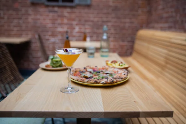 Vegan pizza, a cocktail, and other vegan dishes on a wooden restaurant table — Stockfoto