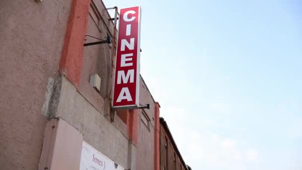 Letrero de cine colgando fuera de un edificio marrón bajo un cielo azul brillante — Vídeo de stock