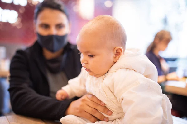 Bebê sentado em uma mesa de restaurante, enquanto sua mãe a segura por sua perna — Fotografia de Stock