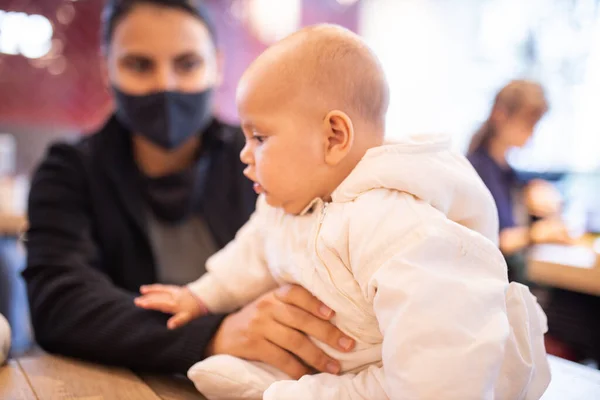 Bebê sentado em perfil em uma mesa ao lado de sua mãe dentro de um restaurante — Fotografia de Stock