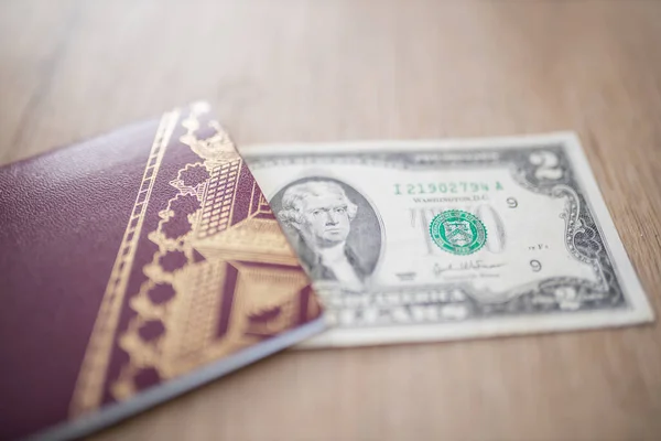 Twee Dollar Bill gedeeltelijk in een Zweeds paspoort op een houten tafel — Stockfoto