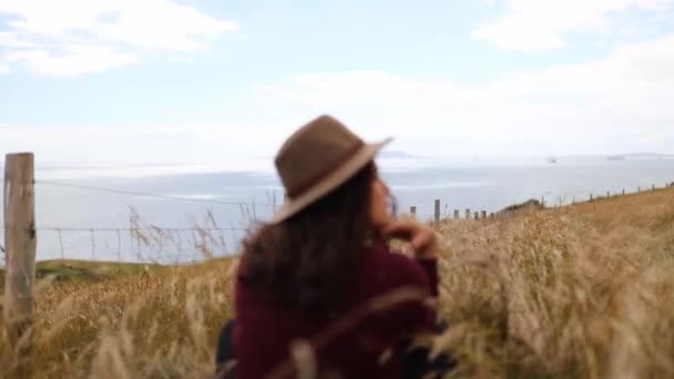 Mujer Descansando en Hierba Seca Alta con el Océano como Fondo — Vídeos de Stock