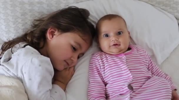 Маленькая девочка отдыхает на кровати со своей счастливой младшей сестрой — стоковое видео