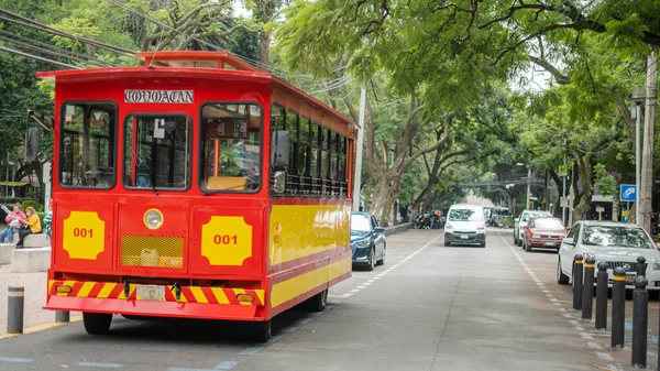 Czerwony i żółty tramwaj na ulicach otoczony drzewami i samochodami — Zdjęcie stockowe