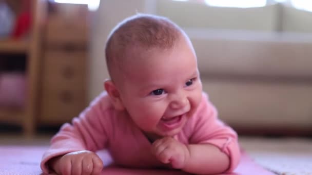 Lächelndes Baby, das mit den Fingern im Mund auf einem rosafarbenen Teppich liegt — Stockvideo