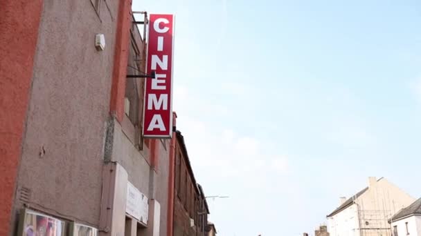 Panneau de cinéma suspendu à l'extérieur d'un bâtiment brun sous un ciel bleu vif — Video