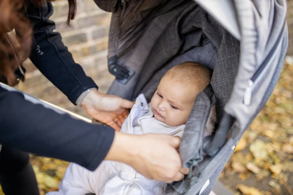 Bebê olha para os braços de sua mãe enquanto ela tenta levantá-la de um carrinho — Fotografia de Stock