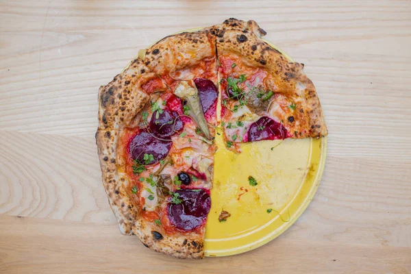 Above view of a thick vegan pizza on a yellow plate with two slices missing — Stockfoto