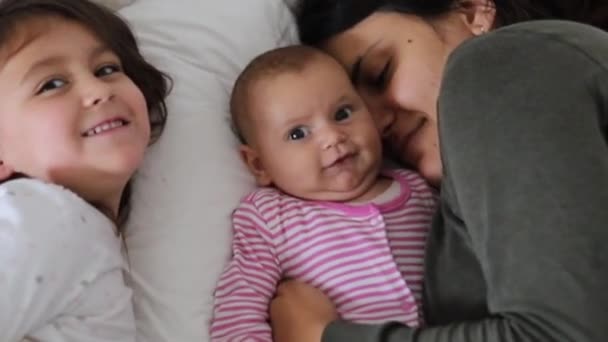 Madre descansando en una cama con sus dos jóvenes y felices hijas — Vídeo de stock