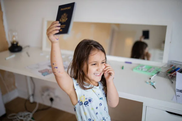 Little girl in front of a desk lifting an American passport high above her head — Stock fotografie