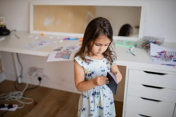 Little girl looking at an American passport with a desk and a mirror behind her — Stock fotografie