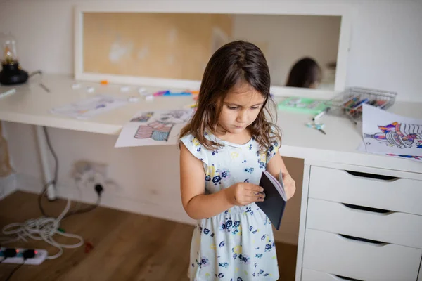 Little girl looking at an American passport with a desk and a mirror behind her — Stock fotografie