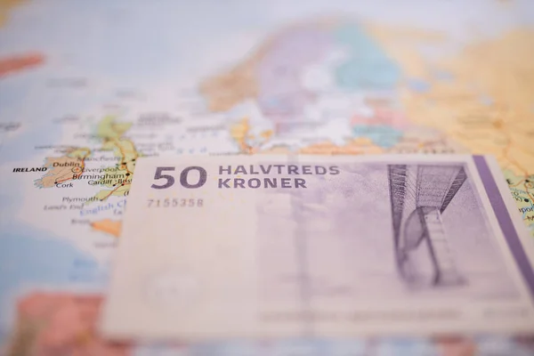 Fifty Danish kroner bill below Denmark on a colorful and blurry Europe map