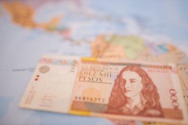 Ten thousand Colombian pesos bill below Colombia on a colorful and blurry map