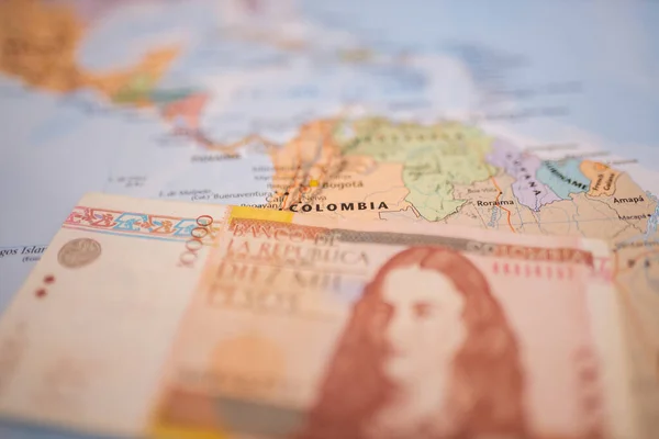 Ten thousand Colombian pesos bill below Colombia on a colorful and blurry map
